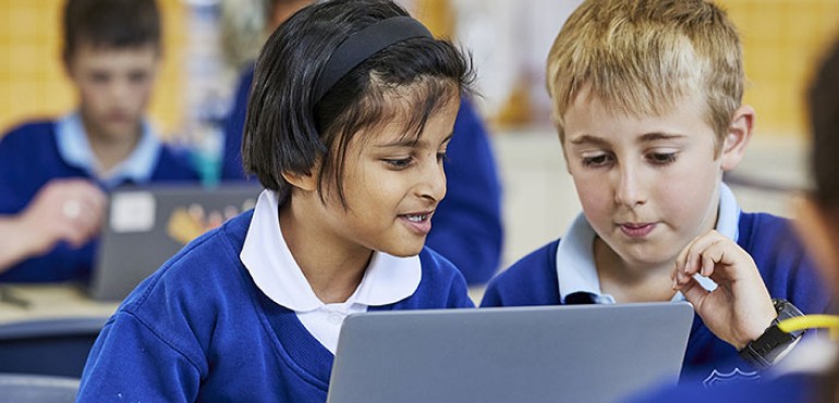 Two students sitting at a classroom desk with a laptop.